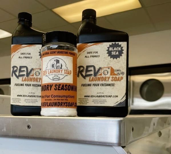 Two 32 fl oz bottles of Rev Laundry Soap, one labelled Black Sea, beside a tub of Rev Laundry Seasoning scent-boosting powder